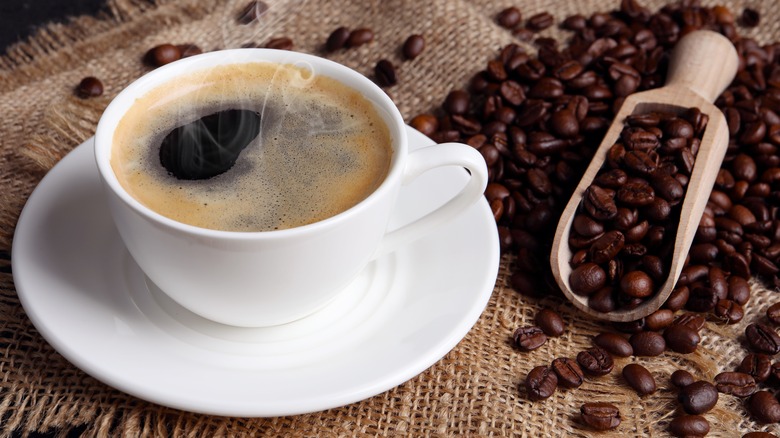 Steaming cup of coffee besides roasted coffee beans.