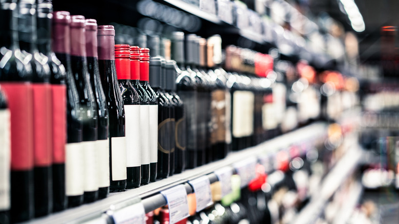 Red wine on a shelf with supermarket aisles in the background.