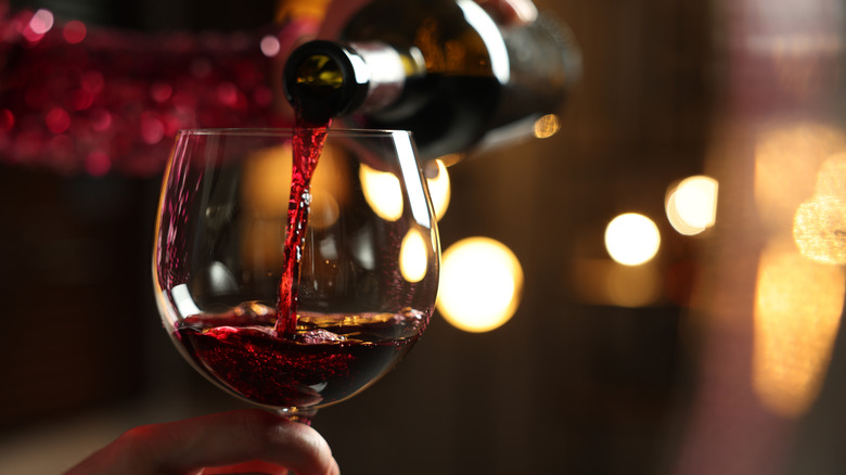 Pouring red wine into a glass with soft lights in the background.