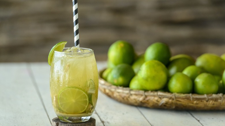 chilled caipirinha with striped straw and basket of limes