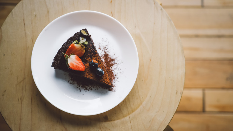 Overhead view of flourless chocolate cake slice topped with berries and cocoa powder.