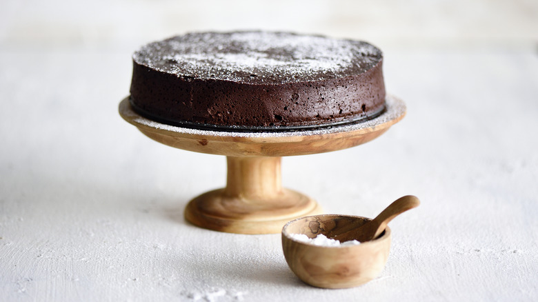 Flourless chocolate cake on wood stand, white background.