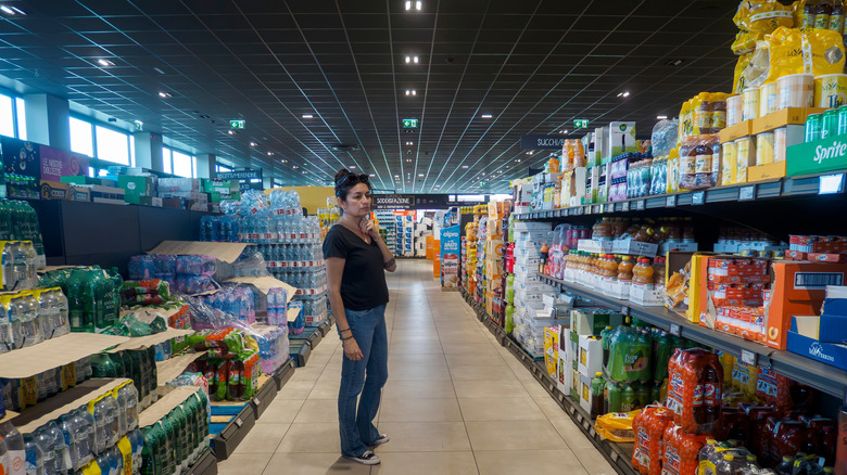 Woman considers products in Aldi drinks aisle.