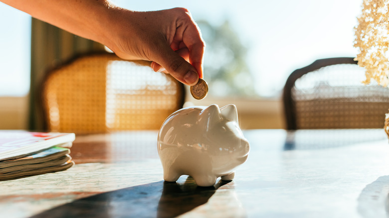 Close-up of someone putting coin in white piggy bank