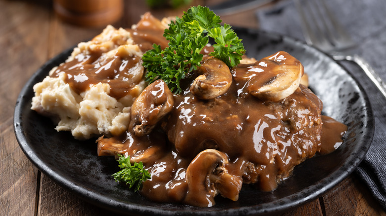 Plate of Salisbury steak with mushrooms, gravy, mashed potatoes, and vegetable garnish