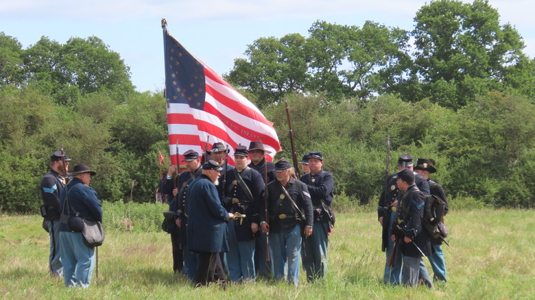 American Civil War reenactors in field with period-accurate American flag.