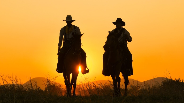 two cowboys on horseback at sunset