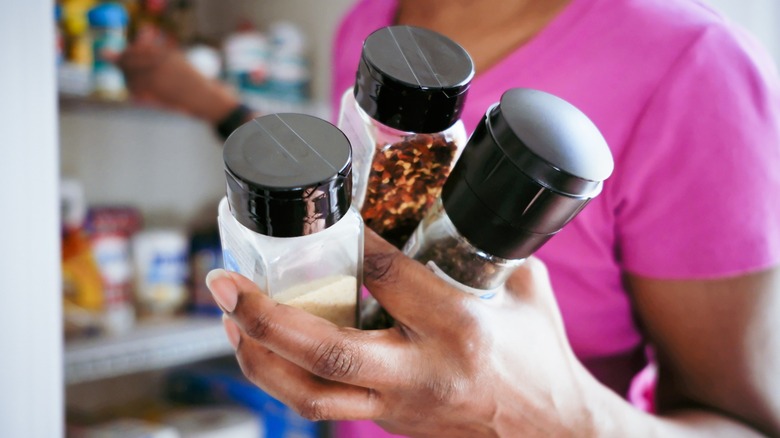 person holds spice bottles in front of pantry