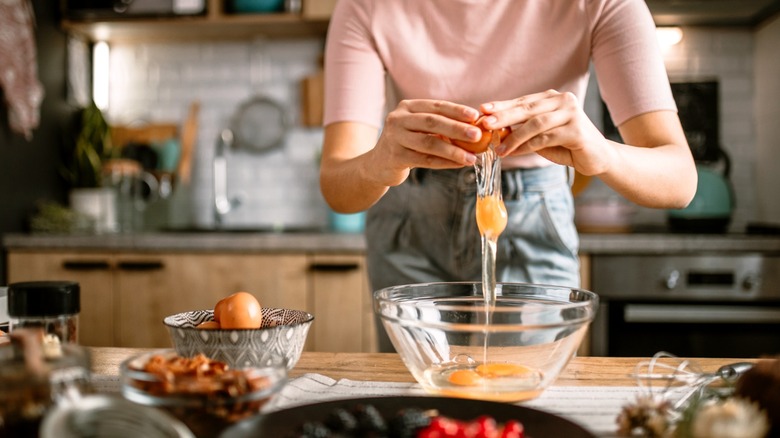 a person cracks eggs in a bowl