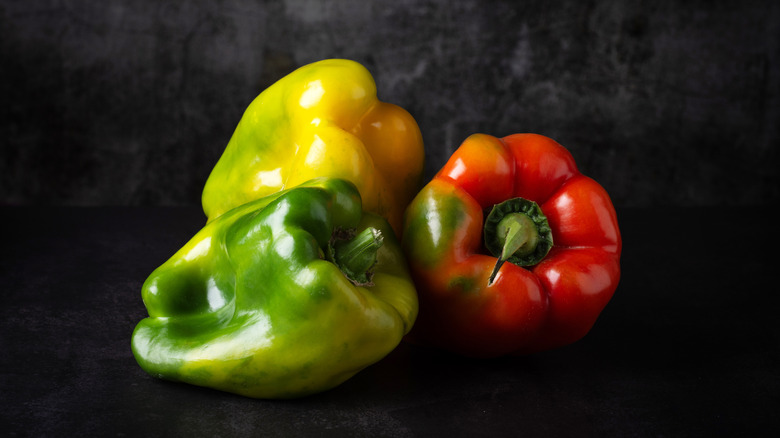 Green, yellow, and red bell peppers on dark background.