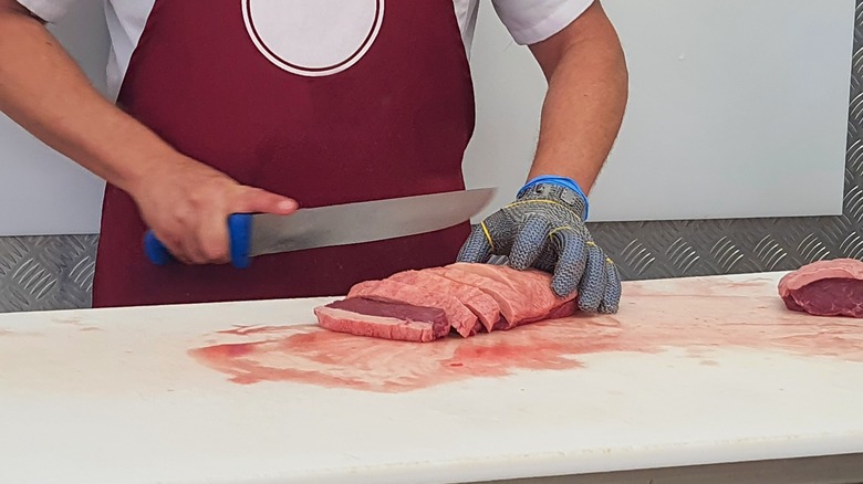 butcher in apron slices red meat on counter
