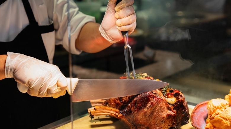 hands carving up a rib roast for prime rib