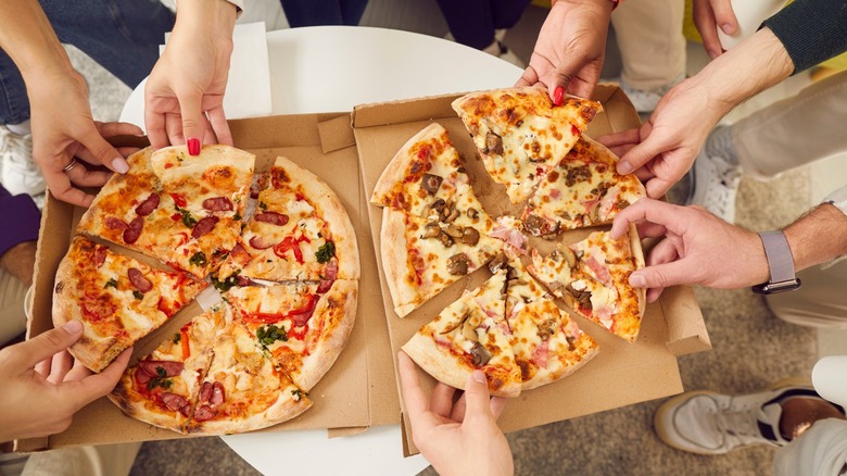 many hands reach for pizza slices from box