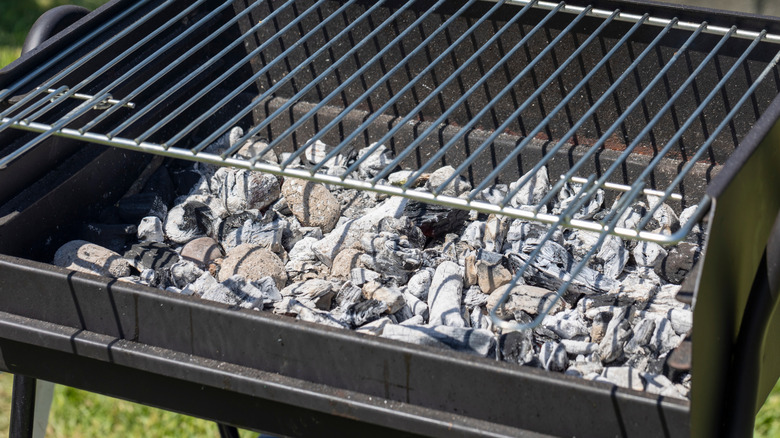 A close-up of a used grill with charcoal and ash in the bottom