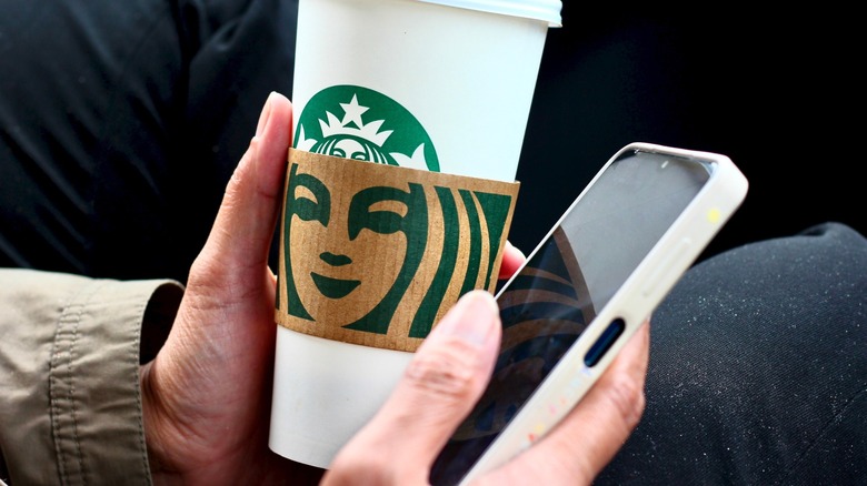 hands hold a phone and a starbucks cup