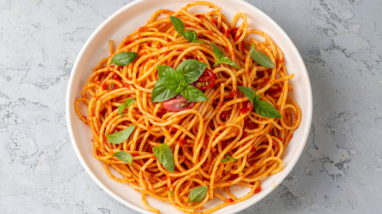 Plate of spaghetti with tomatoes and basil leaves.