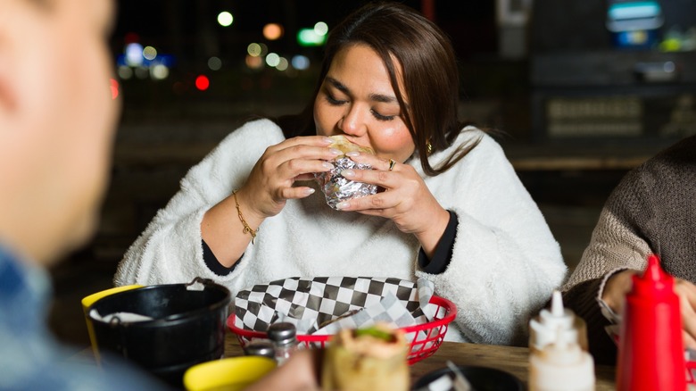 woman eats a burrito over a plastic basket