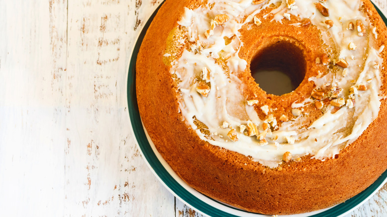 a sock it to me bundt cake with frosting and pecans on top, on a white and green plate