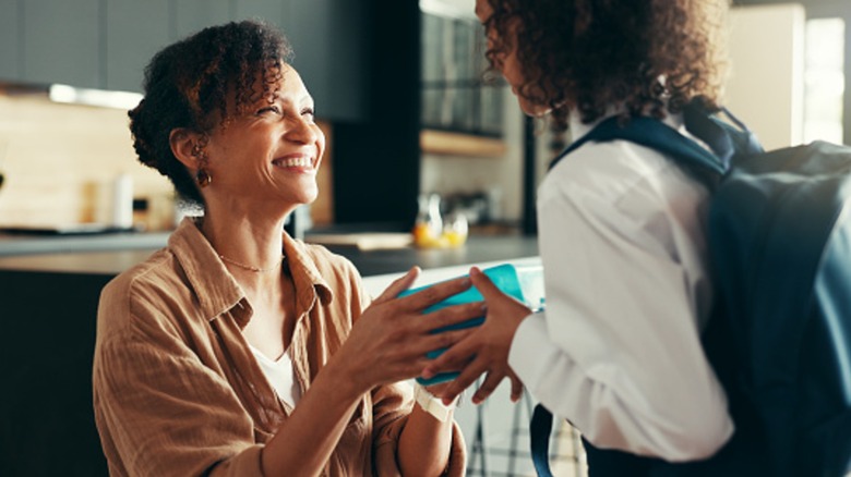 mom hands kid a lunchbox in kitchen