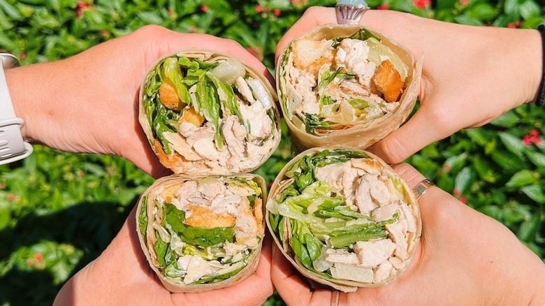 Closeup of two sets of hands holding chicken Caesar salad wraps from Salad and Go