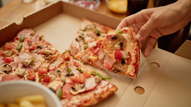 Someone taking a slice of pizza from a box