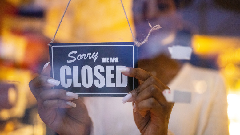 Someone putting a "Sorry we are closed" sign in restaurant window.