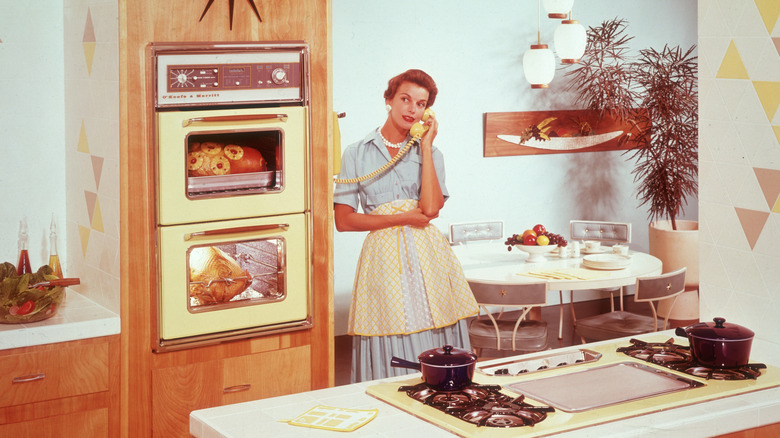 Woman in 1950s kitchen talking on phone.