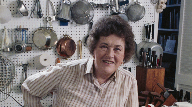 Julia Child sitting in front of lots of kitchen utensils