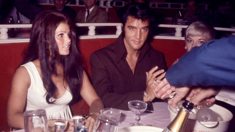 Elvis Presley sits in red booth with champagne