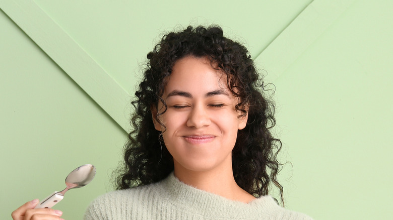 Smiling woman eats dessert standing against green background.