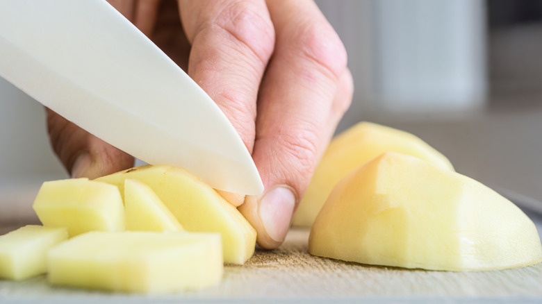 Close up of hands cutting a white potato.