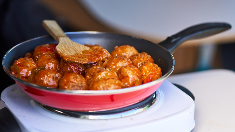 A small pan of meatballs with sauce on a hot plate.