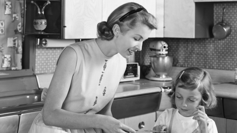 1950s mother and daughter frosting cake in kitchen