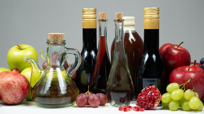 A row of different types of vinegar with fruits like apples and pomegranates