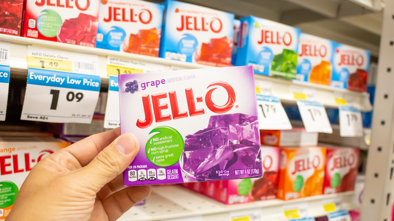 Hand holding package of grape jello in store.