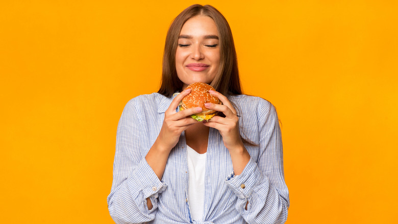 Woman holding hamburger against yellow background.