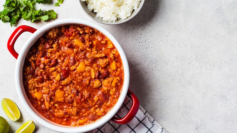pot of chili with rice, lime, and cilantro