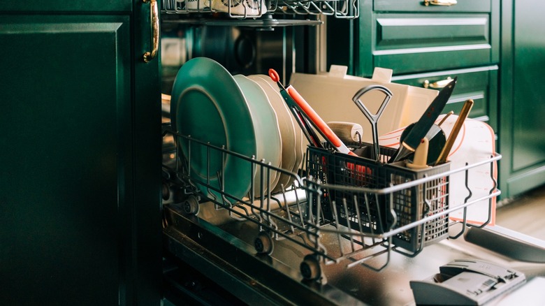 dishwasher installed in green cabinets loaded with dishes