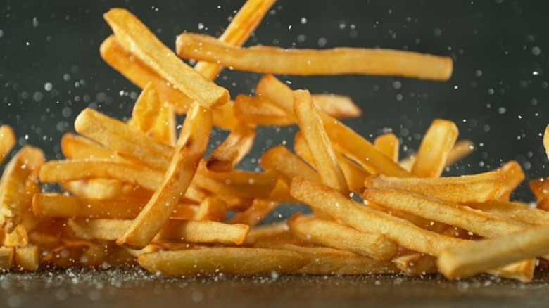 french fries falling in motion amidst salt granules