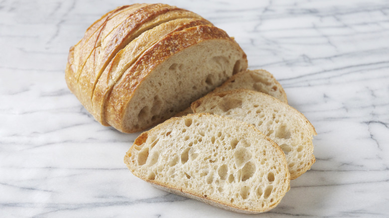 A sliced sourdough loaf on a white and gray marble worktop