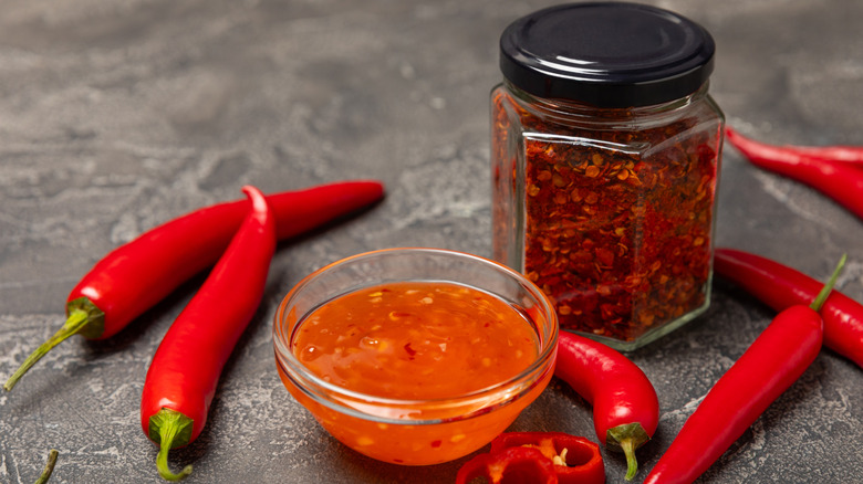 Hot chile sauce in a bowl with fresh red peppers and chile flakes on wooden cutting board