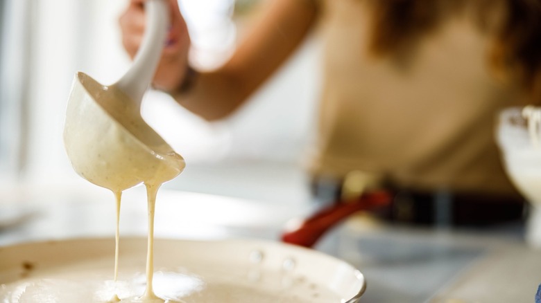 hand ladles pancake mix into skillet