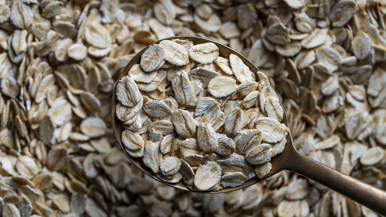 Dry oat flakes in a spoon, with raw oat grains in the background