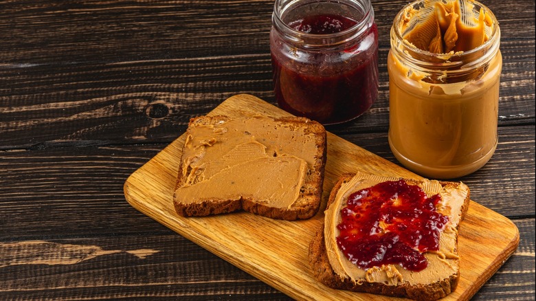 Jars of peanut butter and jelly near bread with the spreads applied