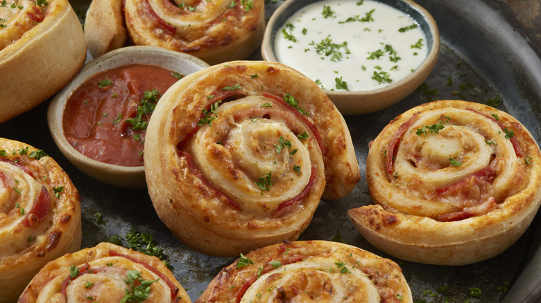 Baked homemade spiral pizza rolls on dark platter with dipping sauces
