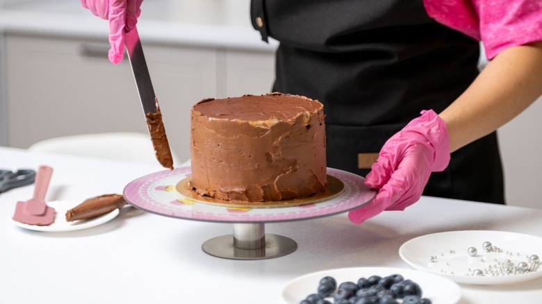 pink gloved hands frost a small chocolate cake