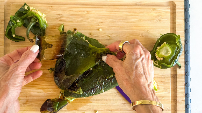 hands peeling poblano pepper skin