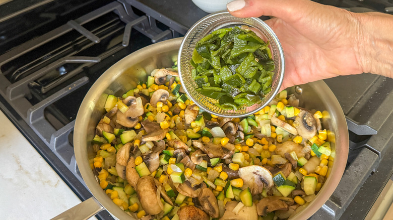 hand adding poblanos to pan with veggie medley