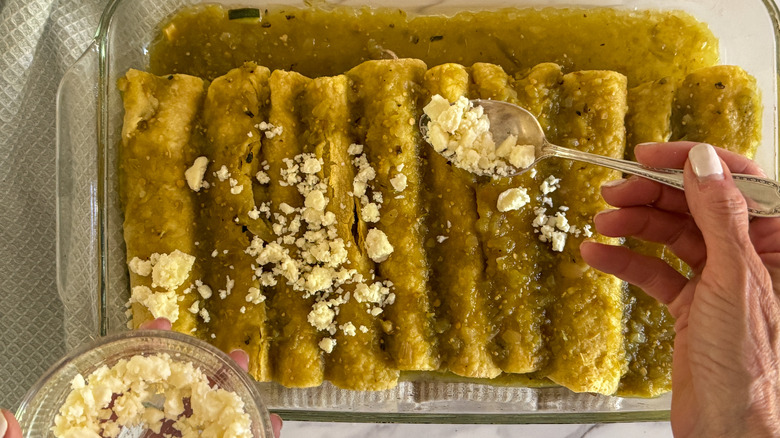 hand sprinkling queso fresco over enchiladas verdes