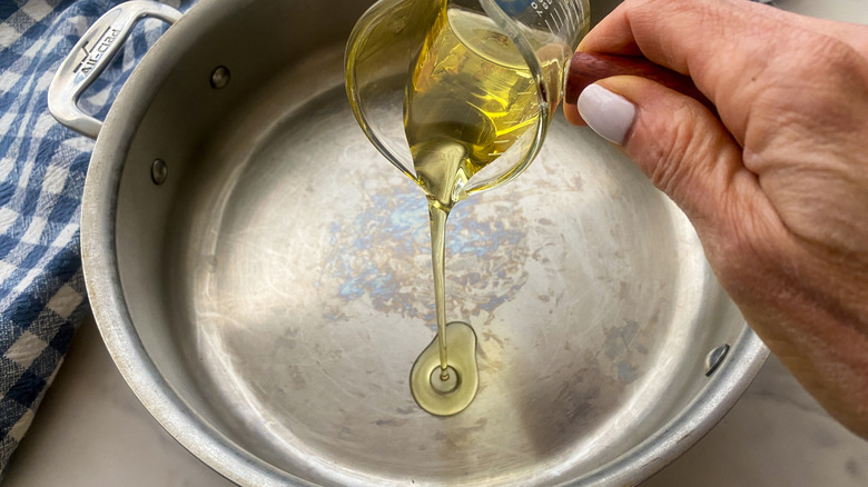 hand adding oil to skillet